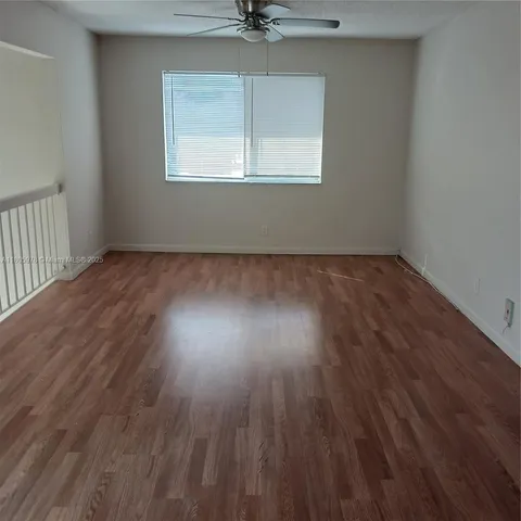 an empty room with wooden floor chandelier fan and windows