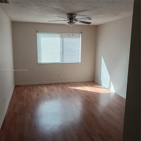 an empty room with wooden floor chandelier fan and windows