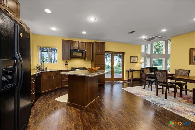 a kitchen with stainless steel appliances granite countertop a refrigerator a stove a sink a dining table and chairs with wooden floor