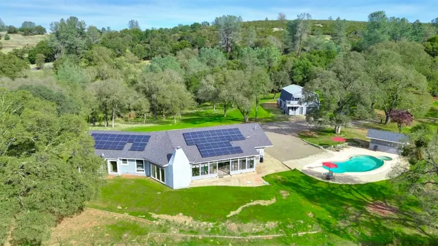an aerial view of a house with pool big yard and large trees