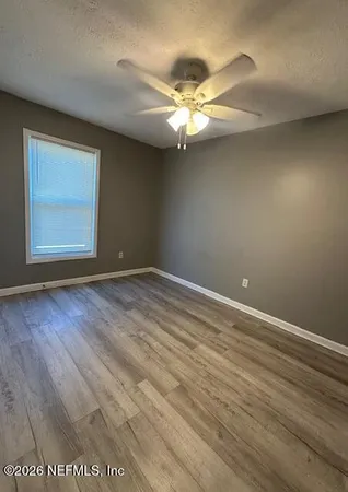 an empty room with wooden floor fan and windows