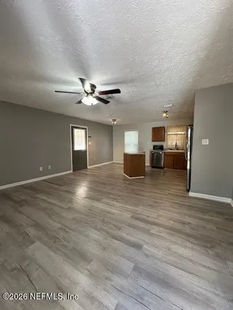 a view of an empty room with wooden floor and a ceiling fan