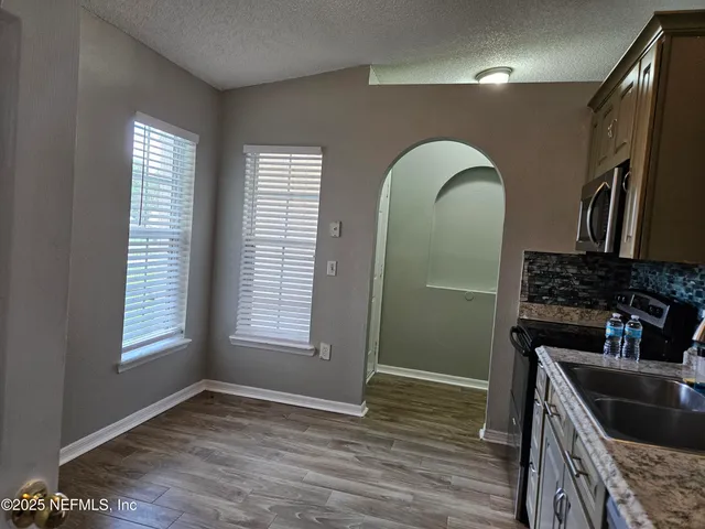 a view of a refrigerator in kitchen and an empty room with wooden floor