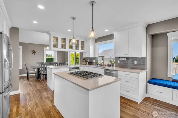 a kitchen with stainless steel appliances kitchen island granite countertop a stove a sink a refrigerator and white cabinets with wooden floor