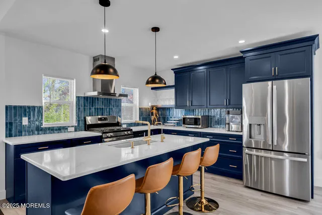 a kitchen with stainless steel appliances a sink a stove a refrigerator and chairs