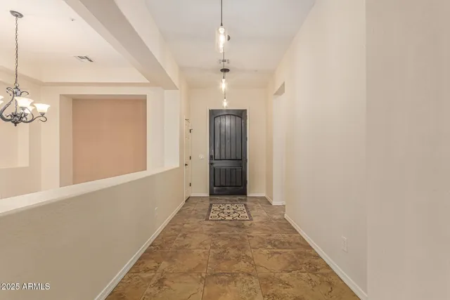 a view of an empty room with chandelier fan and kitchen view
