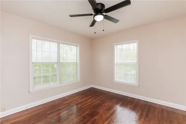 an empty room with wooden floor ceiling fan and windows