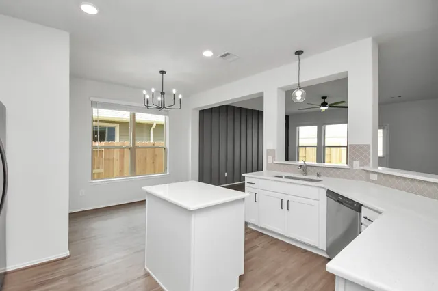 a large white kitchen with a sink dishwasher a stove and white countertops with wooden floor