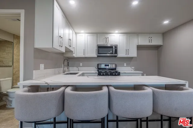 a kitchen with stainless steel appliances granite countertop a sink a stove a refrigerator with white cabinets and couches