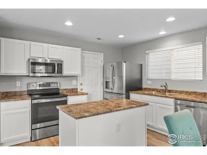 a kitchen with stainless steel appliances granite countertop a stove a sink a microwave a refrigerator and white cabinets