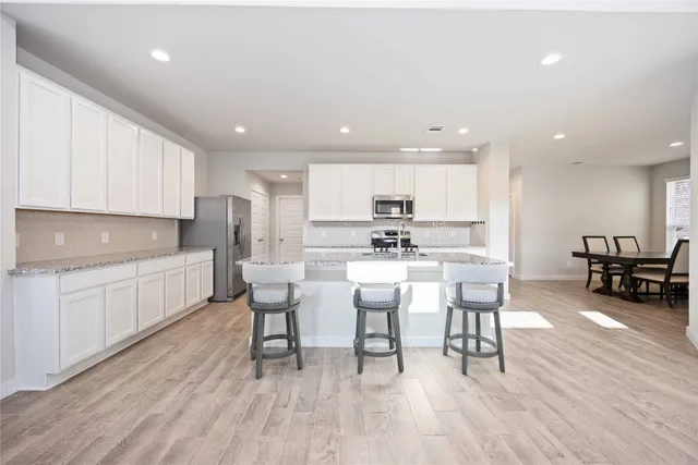 a kitchen with a dining table chairs wooden floor cabinets and appliances
