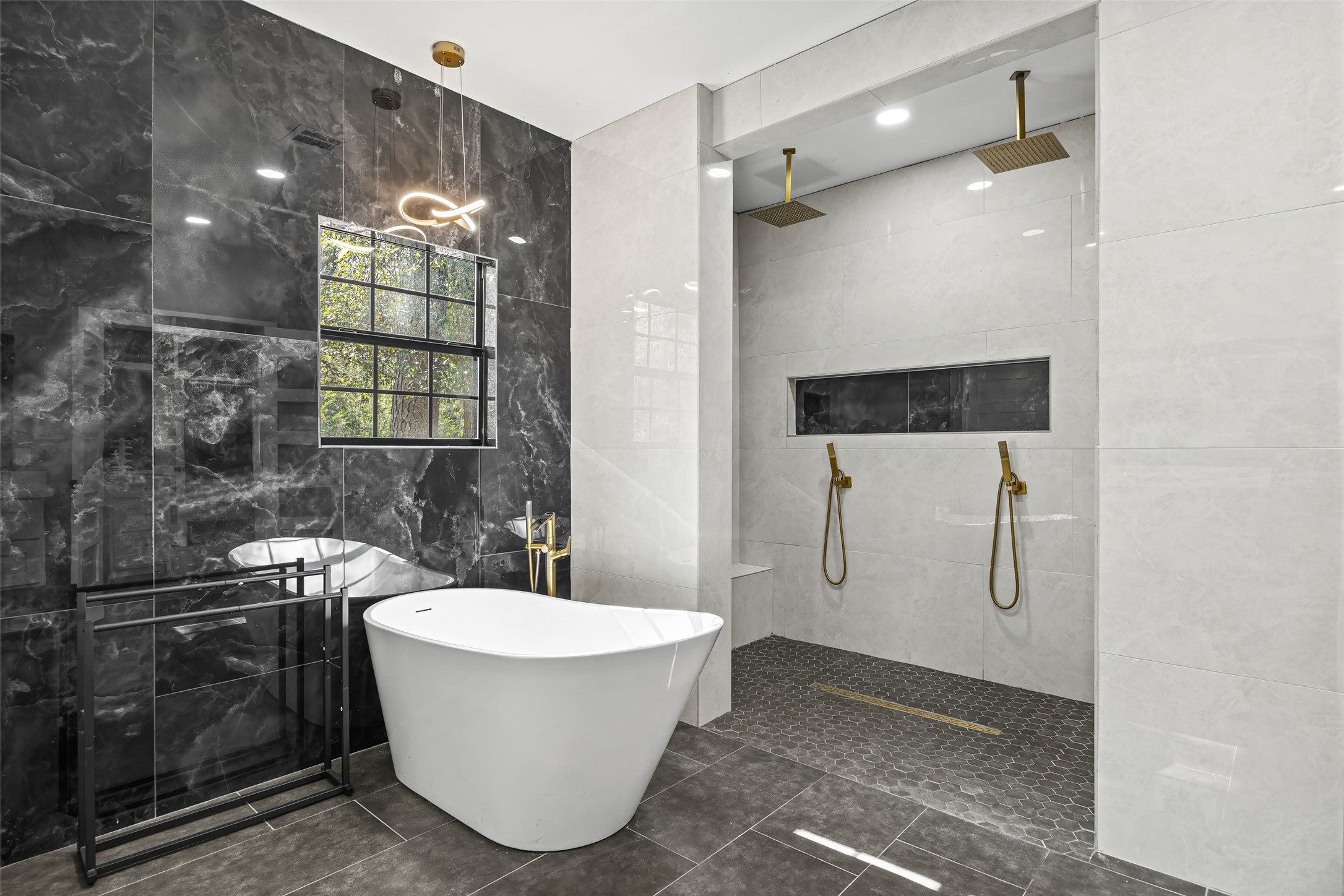 15080 Usher Lane Splendora, TX 77372 - Photo 2 of 44 This luxurious bathroom features a sleek freestanding bathtub against a stunning black marble accent wall, complemented by a modern light fixture. It includes a spacious walk-in shower with dual rain showerheads, elegant brass fixtures, and a stylish tiled floor.