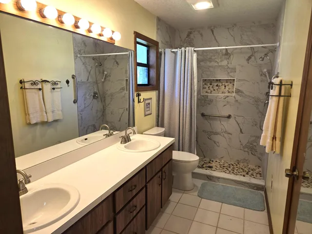 a bathroom with a double vanity sink toilet mirror and shower