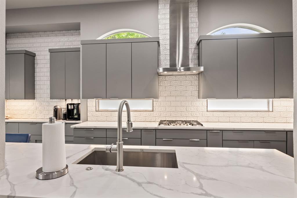 Kitchen with stainless steel gas stovetop, gray cabinetry, modern cabinets, and wall chimney exhaust hood