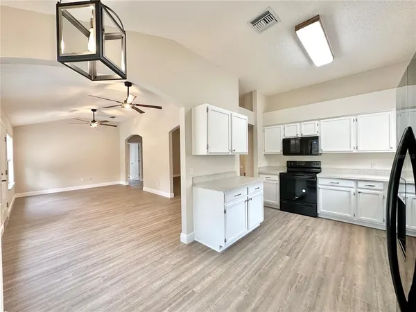 a kitchen with granite countertop a refrigerator oven a sink dishwasher and white cabinets with wooden floor