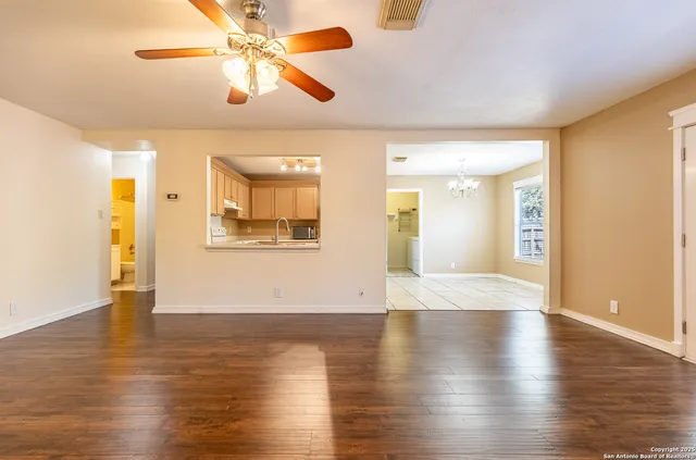 a view of an empty room with wooden floor and a ceiling fan