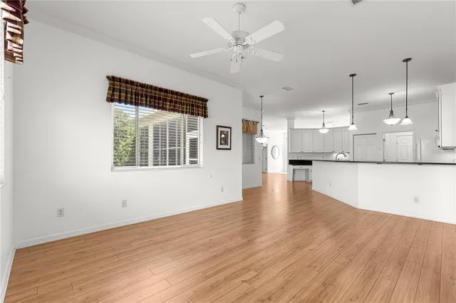 a view of an empty room with wooden floor and a kitchen