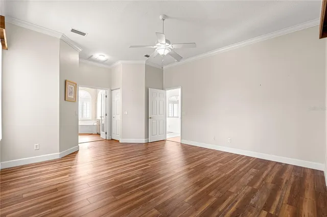 a view of an empty room with wooden floor and a ceiling fan