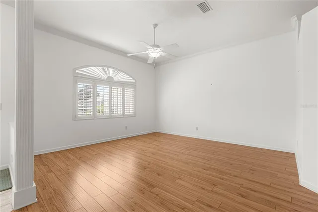 an empty room with wooden floor chandelier fan and windows