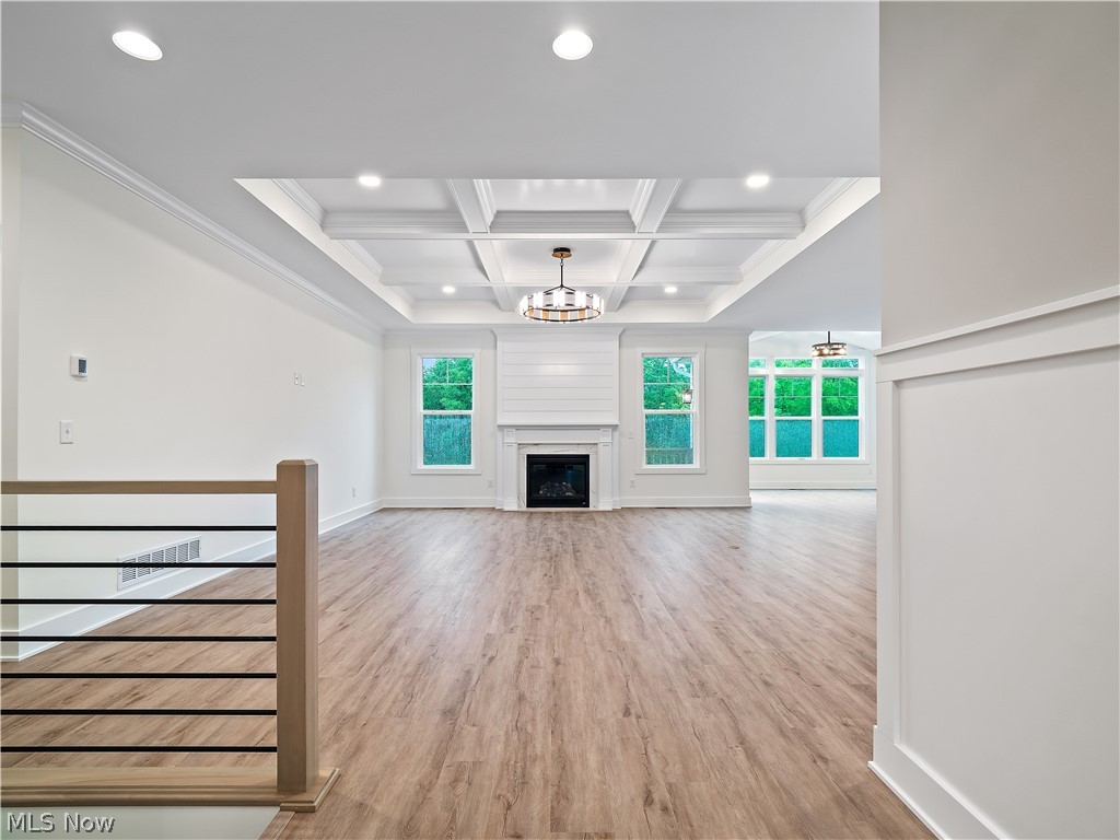 32 Brookside Lane North Ridgeville, OH 44039 - Photo 19 of 50 Unfurnished living room featuring light wood-style floors, beam ceiling, coffered ceiling, a chandelier, and a fireplace