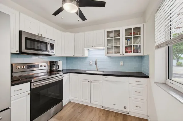a kitchen with granite countertop white cabinets stainless steel appliances and a window