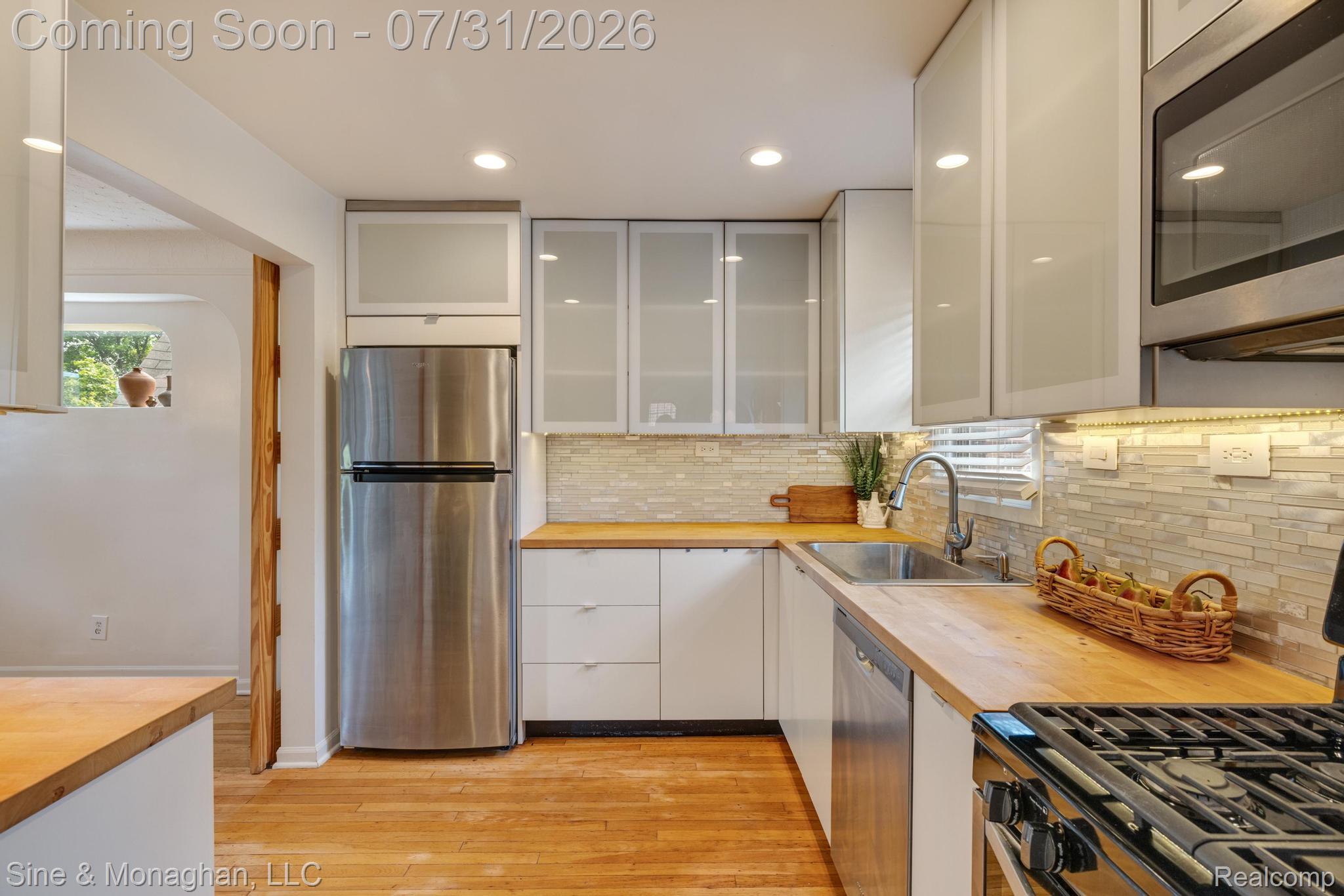 417 Cloverly Road Grosse Pointe, MI 48236 - Photo 17 of 70 Kitchen featuring wood-finish flooring, light wood countertops, a tiled backsplash, contemporary white cabinetry, and stainless steel appliances