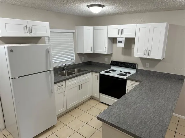 a kitchen with granite countertop a refrigerator a sink and white cabinets
