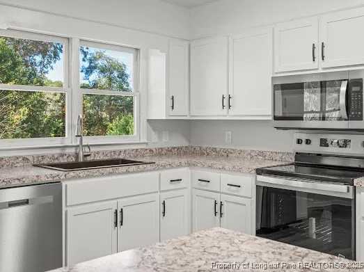 a kitchen with granite countertop a sink stainless steel appliances white cabinets and a window