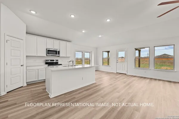 a large white kitchen with granite countertop a stove a sink a refrigerator with white cabinets and wooden floor