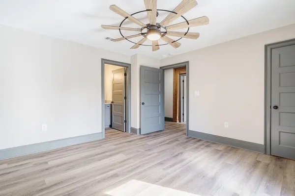 an empty room with wooden floor fan and windows