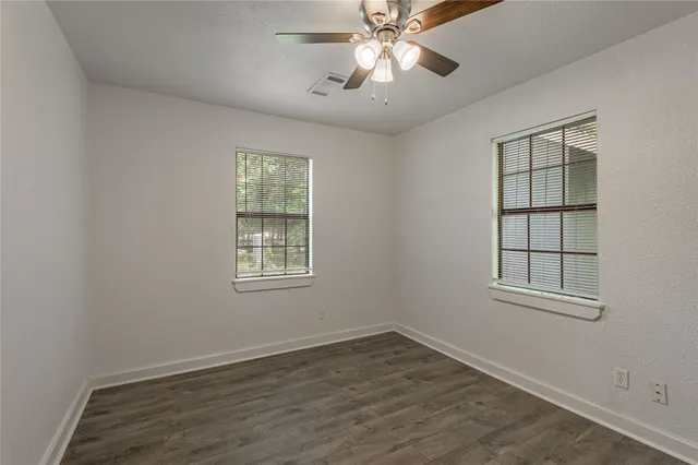 an empty room with wooden floor closet and windows