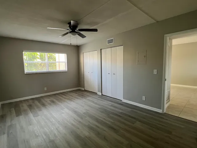 an empty room with wooden floor chandelier fan and windows