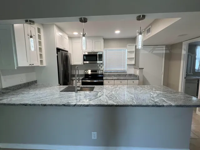 a kitchen with stainless steel appliances granite countertop a sink a stove a refrigerator a washer dryer and a refrigerator