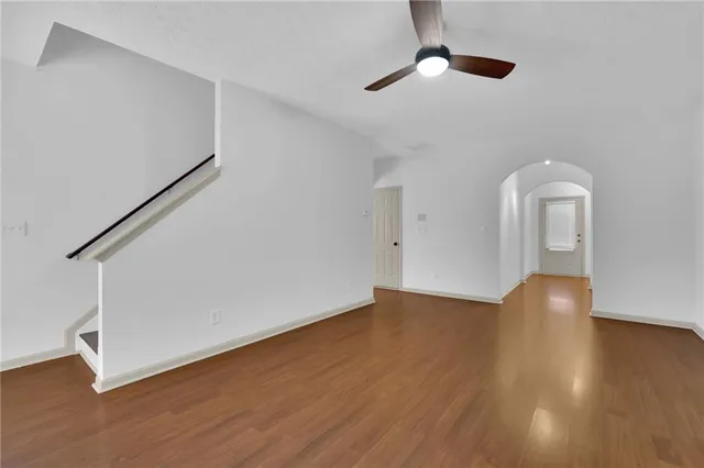 a view of an empty room with wooden floor and a ceiling fan