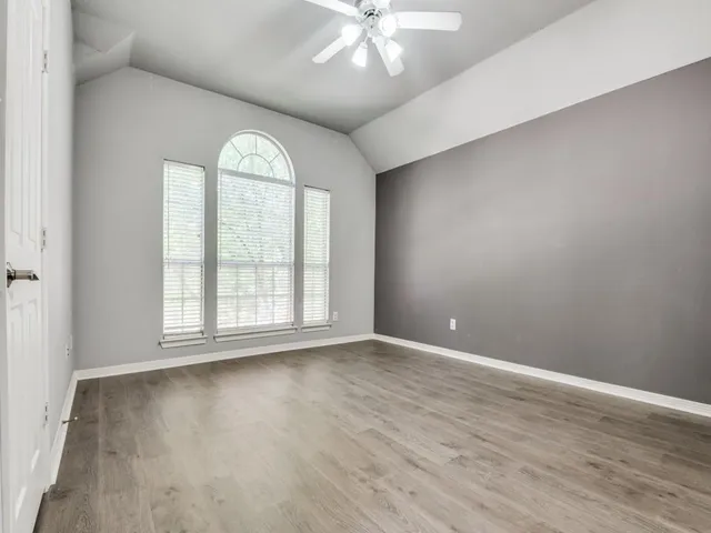 an empty room with wooden floor fan and windows