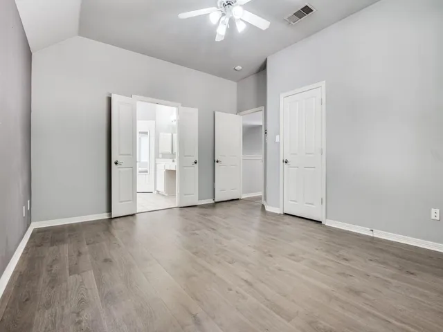 a view of an empty room with wooden floor and a ceiling fan