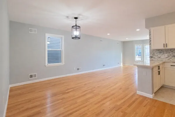a view of empty room with wooden floor and kitchen view