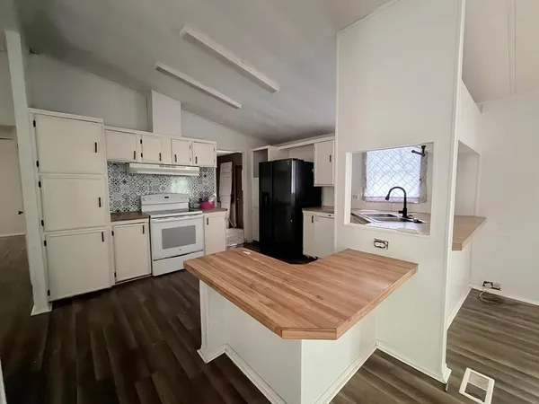 a view of a refrigerator in kitchen and an empty room with wooden floor