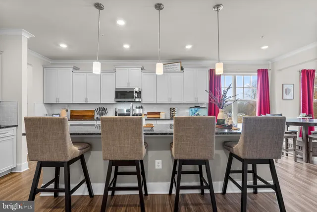 a kitchen with a dining table chairs wooden floor cabinets and a refrigerator