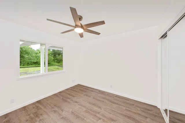 a view of empty room with wooden floor and fan