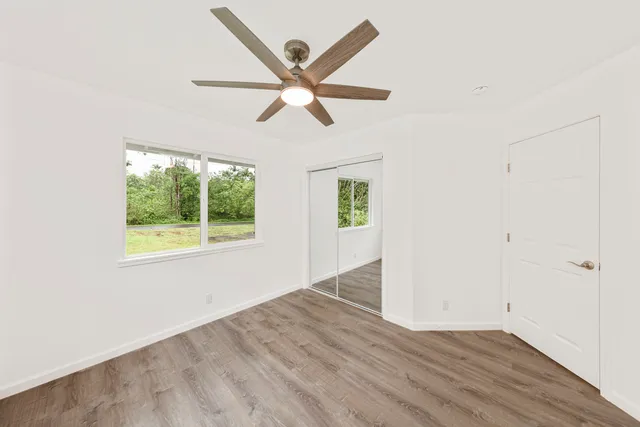 an empty room with wooden floor fan and windows