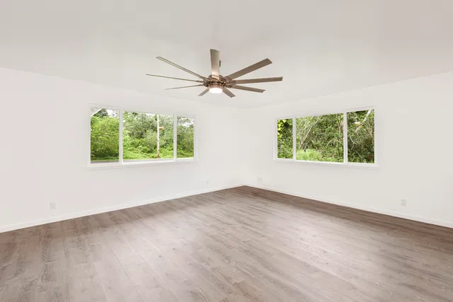 an empty room with wooden floor ceiling fan and windows