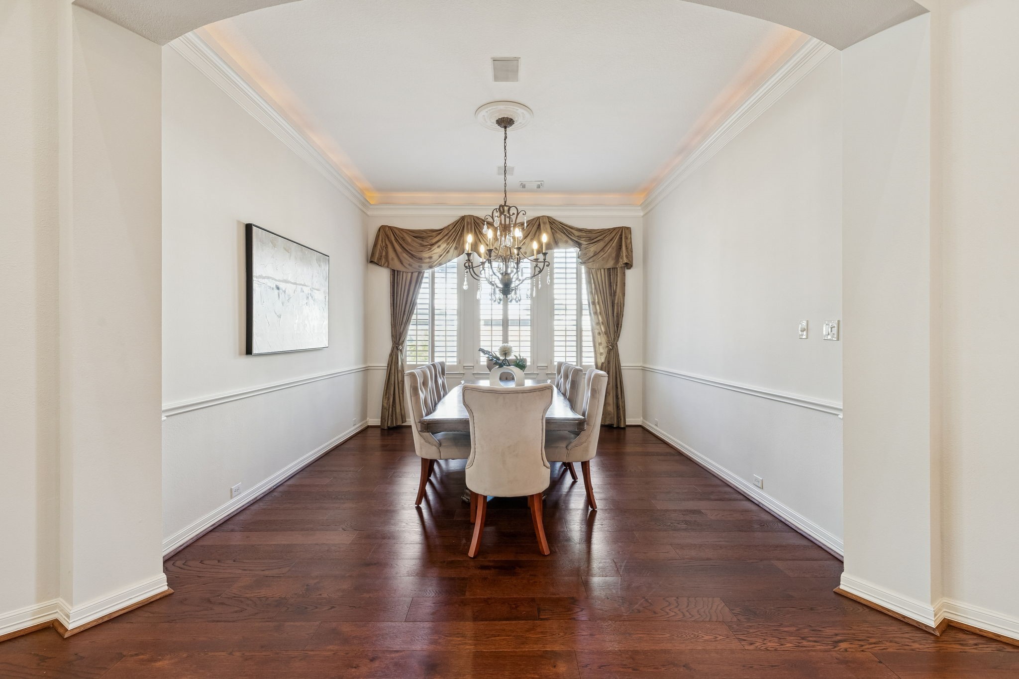 2202 Britton Ridge Drive Katy, TX 77494 - Photo 11 of 41 Elegant formal dining room framed by a graceful archway, featuring rich engineered wood flooring, a tray ceiling with soft cove lighting, and a statement chandelier—perfect for hosting refined dinners and special occasions.