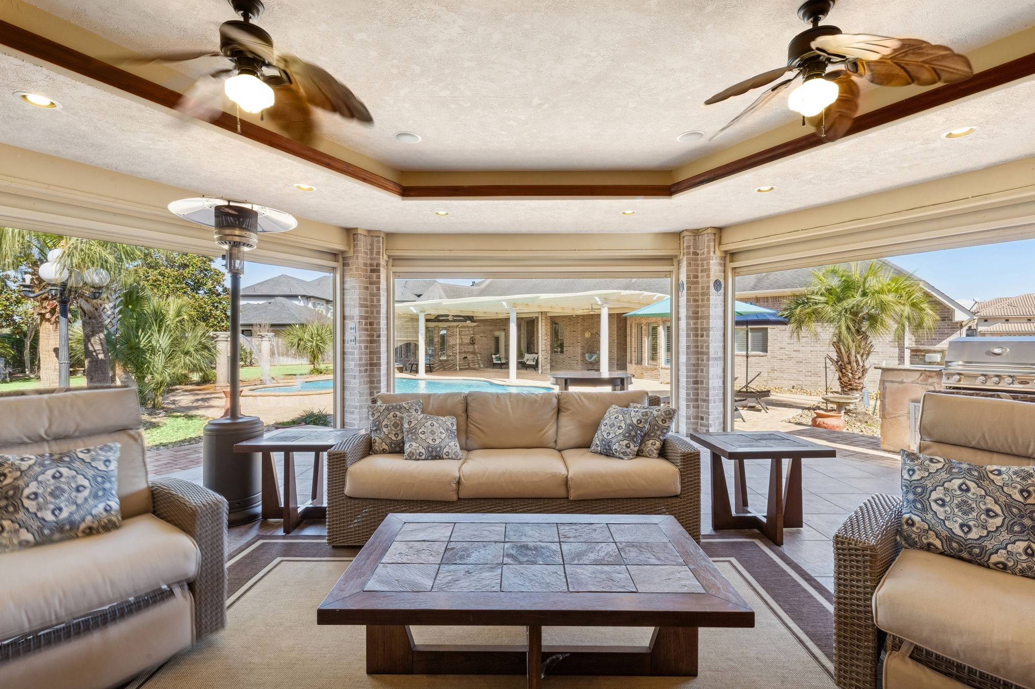2202 Britton Ridge Drive Katy, TX 77494 - Photo 30 of 41 Enclosed outdoor living room from another perspective. Designed for year-round enjoyment, featuring a comfortable lounge area with ceiling fans, heaters, and seamless views of the pool and summer kitchen—perfect for relaxed evenings or entertaining in any season.