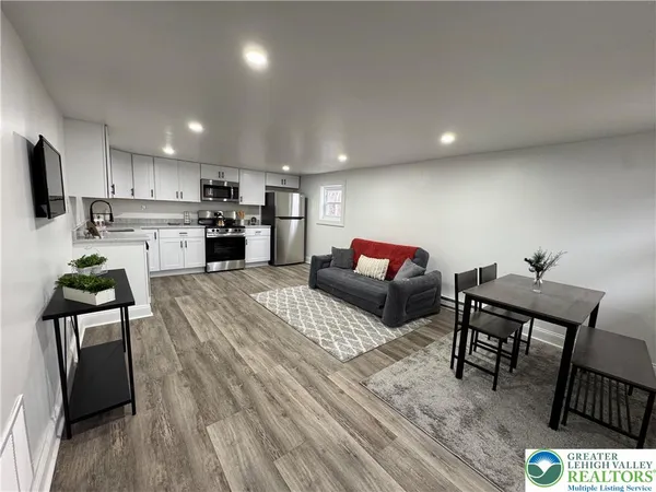a living room with stainless steel appliances furniture wooden floor and a kitchen view