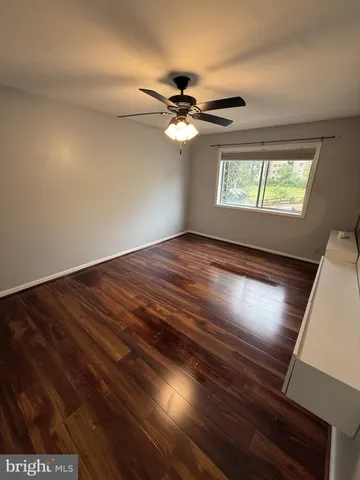 an empty room with wooden floor ceiling fan and windows