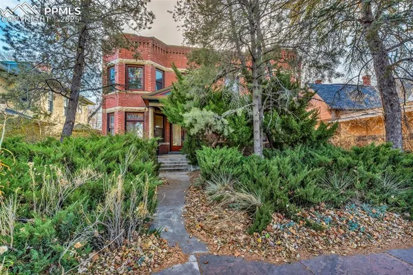 a view of a brick house with lots of plants and large trees