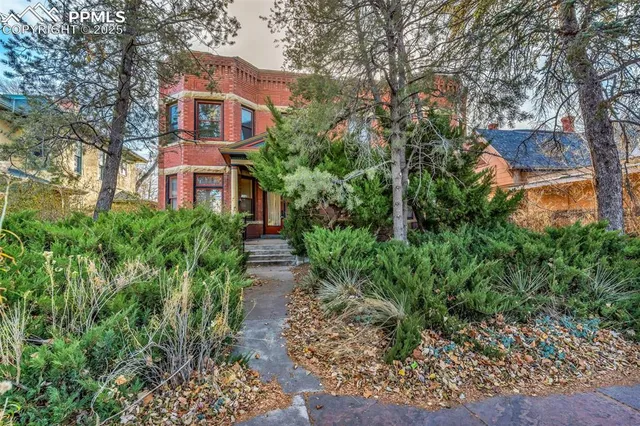 a view of a brick house with lots of plants and large trees