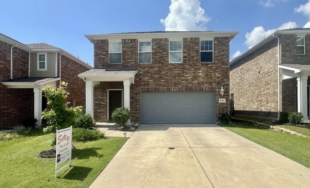 Brick facade two-story residence featuring a covered entry porch with white columns, an attached garage with a gray door, a concrete driveway, and a front lawn with foundational shrubs