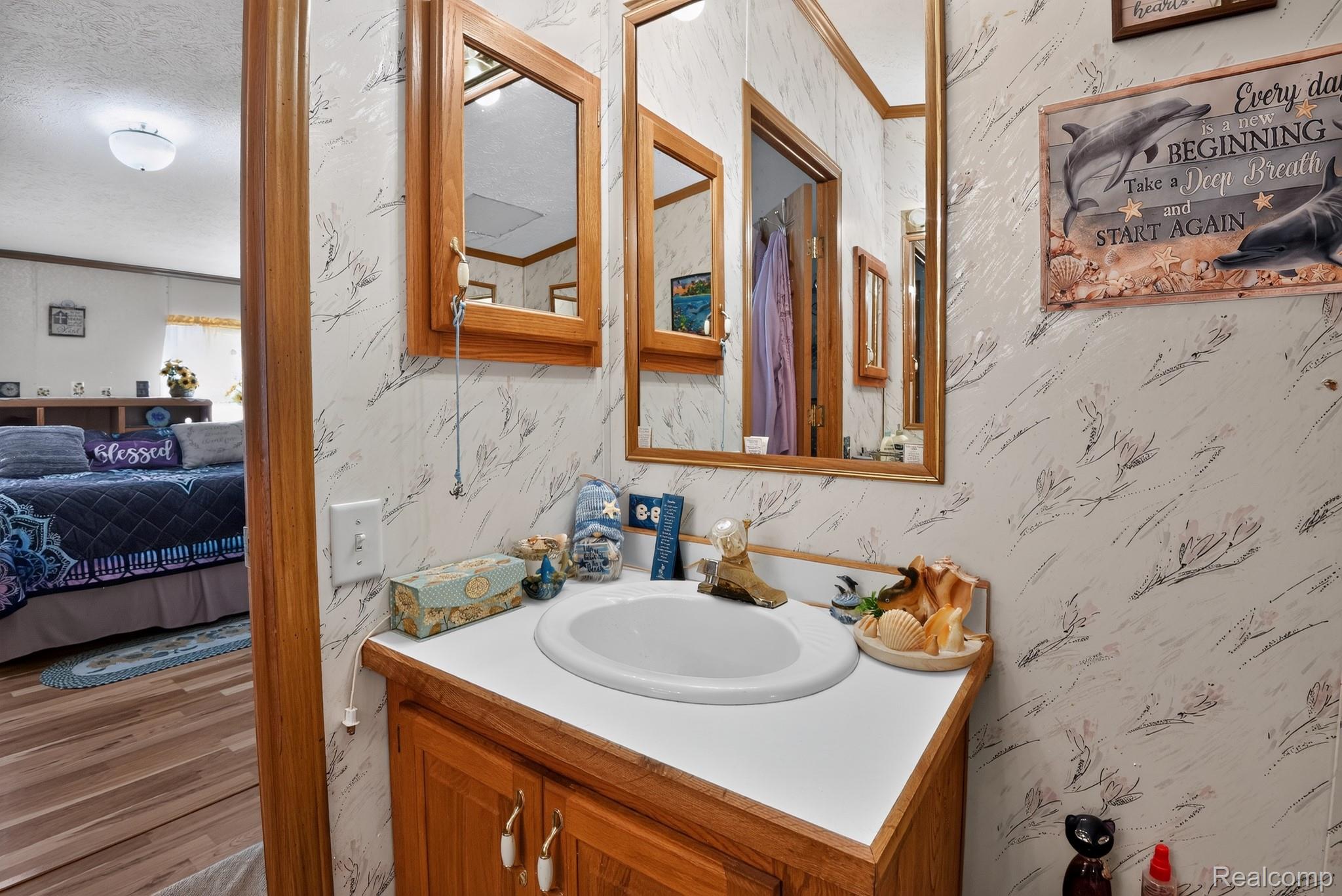 6266 Kikendall Road Eaton Rapids, MI 48827 - Photo 31 of 36 Vanity with a white countertop and integrated sink, wood-finish cabinetry, and a framed wall mirror